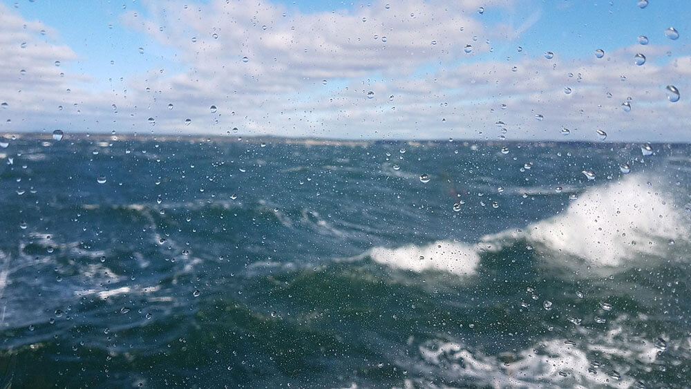 Whitecaps and breaking waves through a sand-encrusted cockpit enclosure