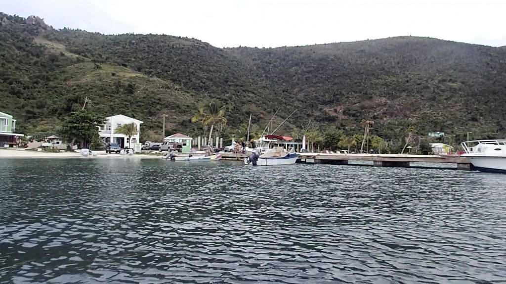 dock with a few island boats tied up and a white building at the head of the dock with mountains rising in the background