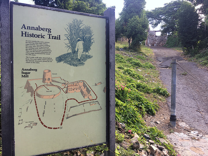 Interpretive sign for Annaberg Historic Trail with path leading up to cobblestone ruins on the right.